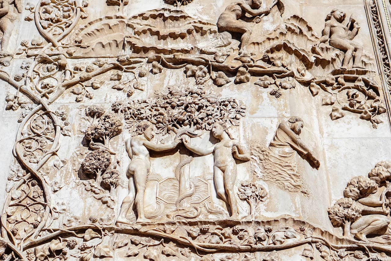 Un dettaglio del morso alla mela di Adamo ed Eva, episodio biblico raffigurato sulla facciata del Duomo di Orvieto con una cornice di tralci di vite
